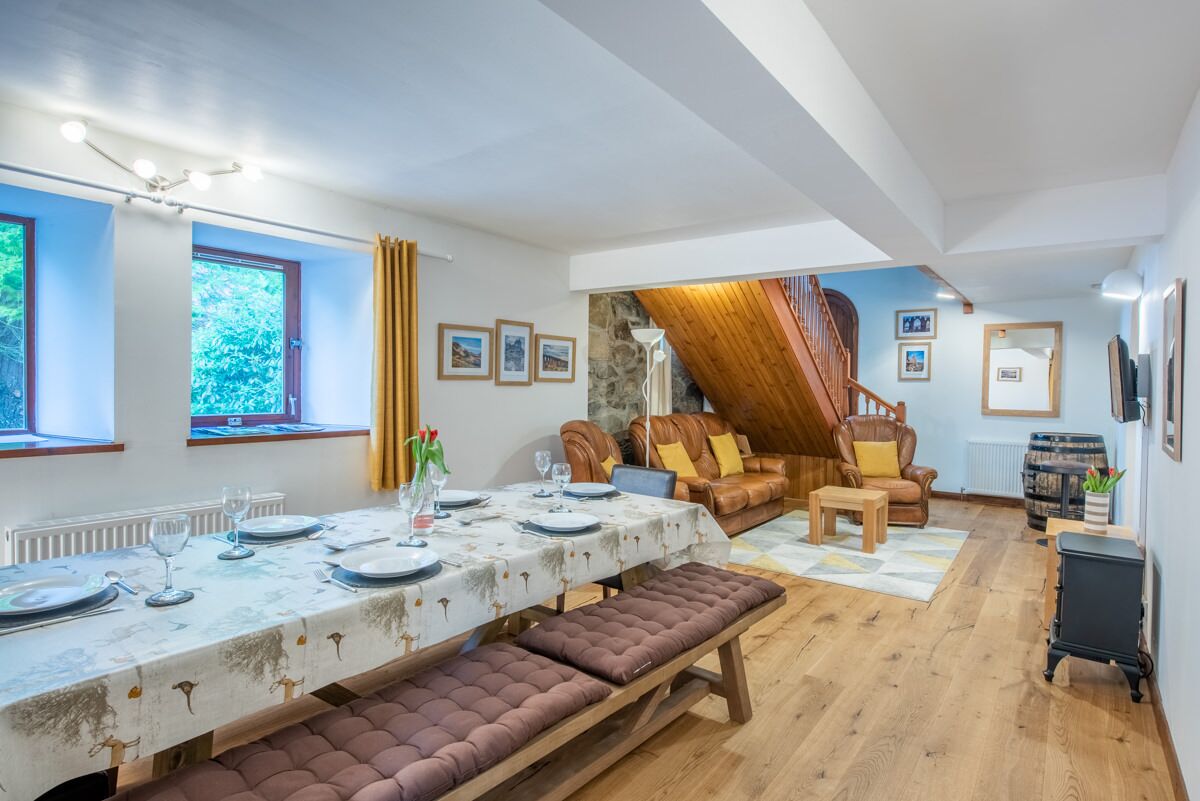 A dining area with a table set for four, a bench, a leather sofa, and a staircase leading to an upper level.