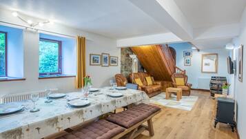 A dining area with a table set for four, a bench, a leather sofa, and a staircase leading to an upper level.