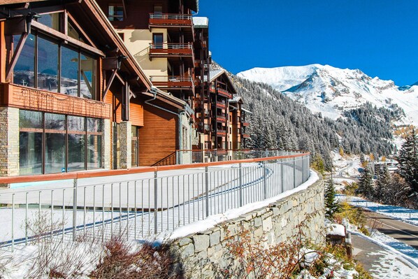 A mountain lodge with multiple balconies, large windows, and a view of snow-covered mountains.