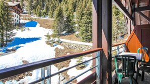 A balcony with a view of a snowy landscape, a wooden building, and a table with chairs. - Cosy, modern 2-bed with fireplace & beautiful views (Flaine)