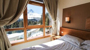A bedroom with a large window, wooden headboard, and a bedside table. - Cosy, modern 2-bed with fireplace & beautiful views (Flaine)