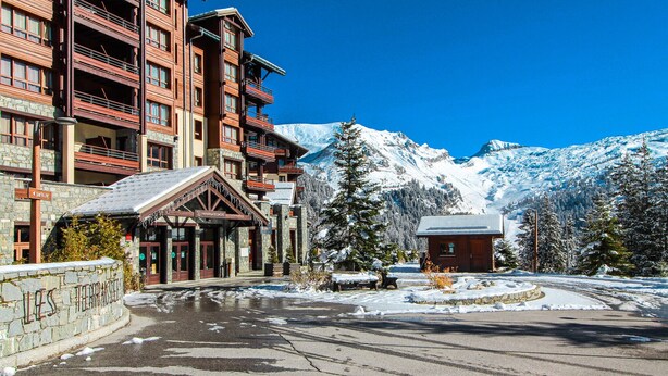 A multi-story hotel with a stone facade, a ski lift, and a snow-covered mountain in the background. - Cosy, modern 2-bed with fireplace & beautiful views (Flaine)