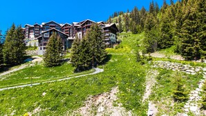Ein mehrstöckiges Hotel mit Balkonen, gelegen an einem Hang mit dichtem Wald und klarem Himmel.