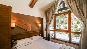 Ein Schlafzimmer mit hölzernem Kopfteil, einem Bett mit weißen Leinen, einem Nachttisch mit Lampe und einem Fenster mit Vorhängen.