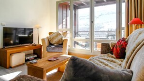 A living room with a television, a wooden coffee table, a sofa, and a large window with a view of a snowy landscape. - South-facing newly renovated 2-bed apartment (Flaine)