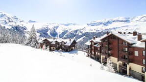 En snötäckt bergsanläggning med stugliknande byggnader, skidbackar och en klar himmel.