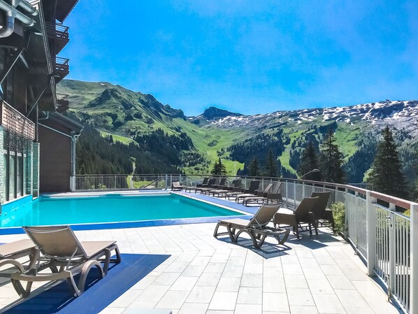 A poolside area with lounge chairs and a view of mountains.