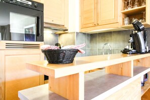 A kitchen with wooden cabinets, a stainless steel range hood, a black coffee maker, and a wicker basket with a cloth on the countertop.