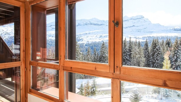 Ein Zimmer mit großen Fenstern und Blick auf schneebedeckte Berge und Bäume.