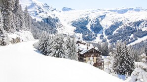 Schneebedeckte Berglandschaft mit einer Berghütte über mehreren Etagen und einer Skipiste im Hintergrund.