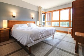 A bedroom with a large bed, nightstands, a wooden bench, and a window with a view of trees. - Stunning 3-bedroom apartment with mountain views (Flaine)