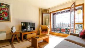 Ein modernes Wohnzimmer mit einer Couch, einem Fernseher, einem Holztisch und einem Balkon mit Bergblick.