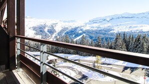 Vista desde un balcón con barandilla de metal, sobre un paisaje nevado con árboles y montañas.