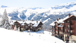 Un complejo turístico en la montaña cubierto de nieve, con edificios de estilo chalet, pistas de esquí y una vista despejada del paisaje nevado circundante.