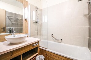 Een badkamer met een houten wastafelmeubel, een witte wasbak, een douchecabine van glas en een wit bad.