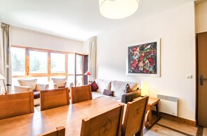 A dining area with a wooden table and chairs, a sofa, and a window with curtains.