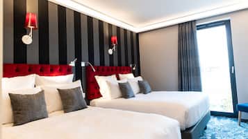 A hotel room with two beds, striped wallpaper, red headboard, and a large window with curtains.