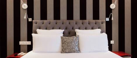 A neatly made bed with white linens and two pillows, a tufted headboard, and two wall-mounted red lamps.