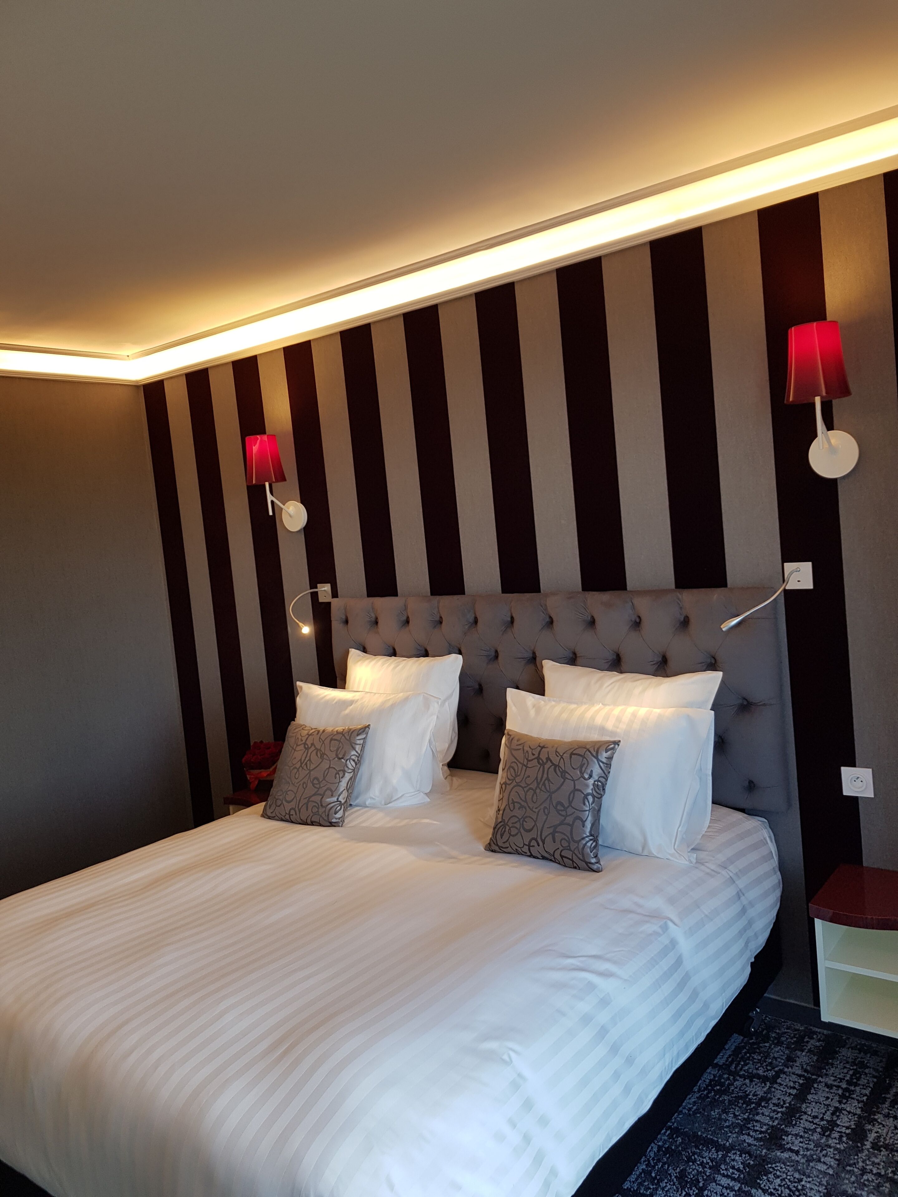 A neatly made bed with white linens, a tufted headboard, and two bedside lamps with red shades.