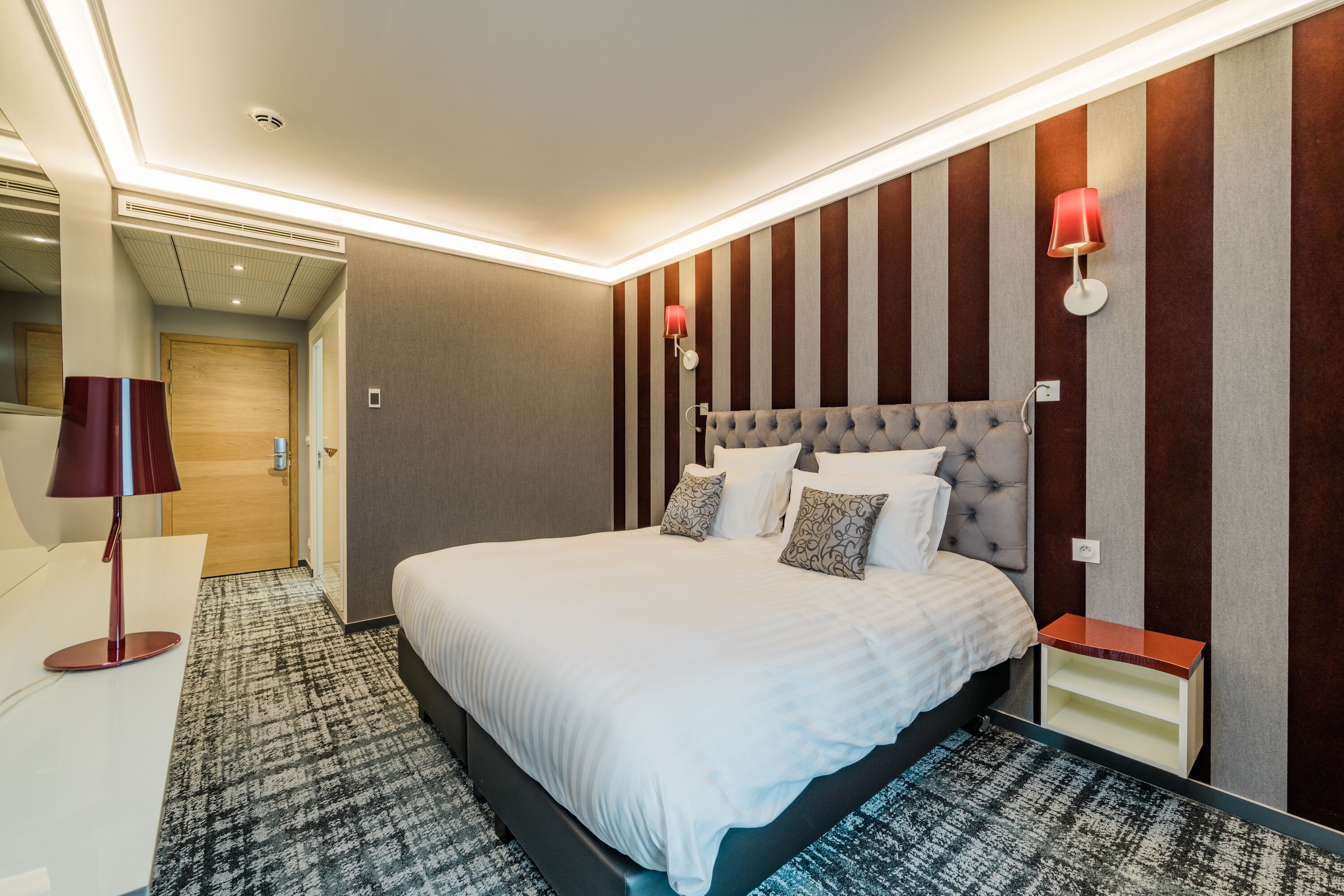 Une chambre d’hôtel moderne avec un grand lit, une table de chevet, une lampe et un luminaire fixé au mur.