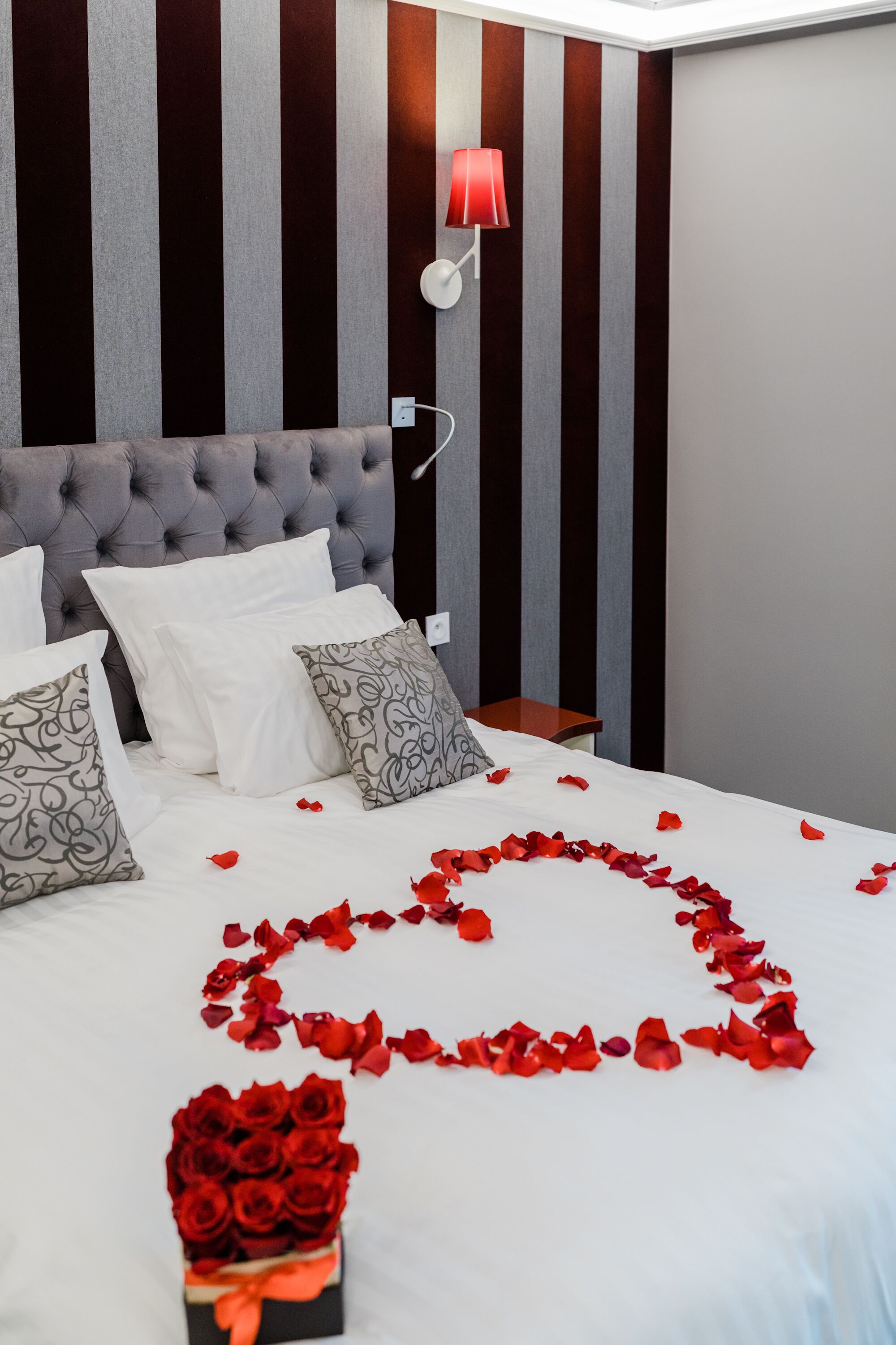 A neatly made bed with white linens and decorative pillows, a bedside table with a lamp, and a wall with vertical stripes.