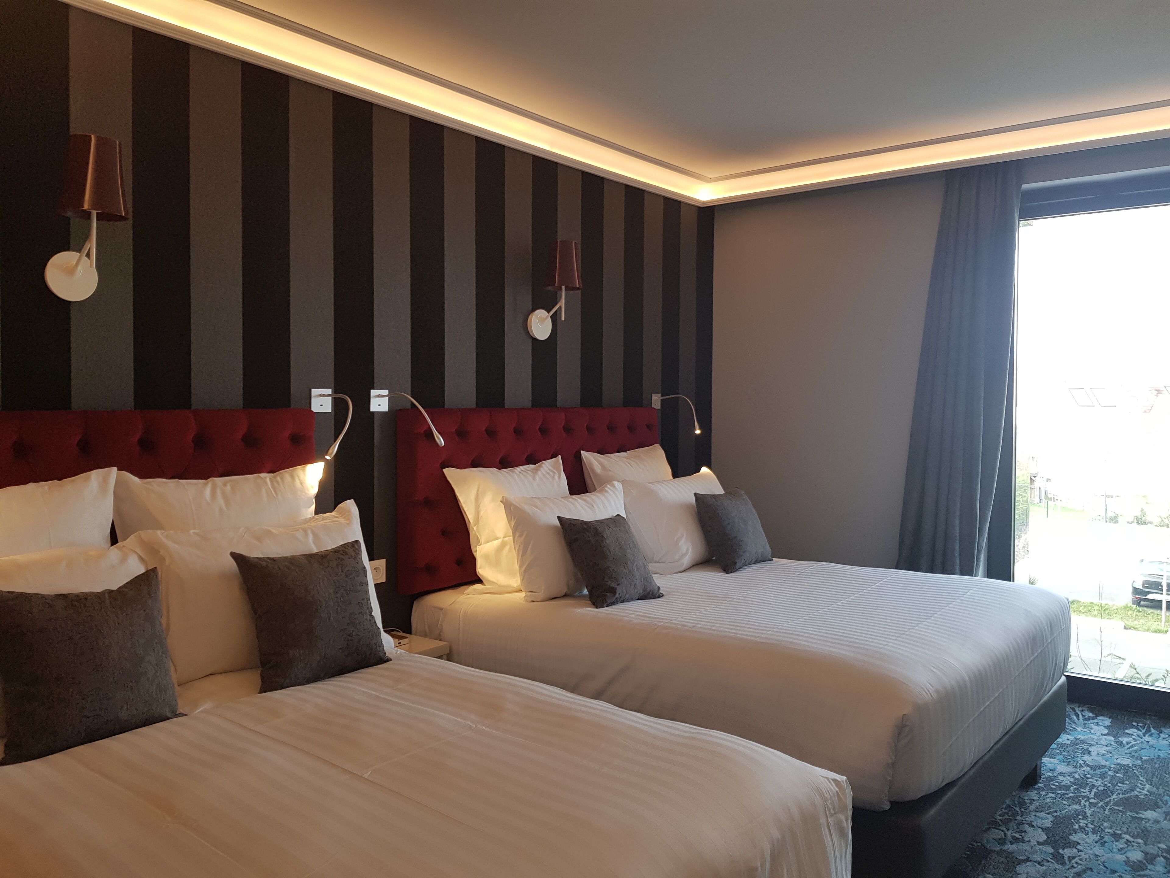 Una habitación de hotel con dos camas, papel tapiz a rayas y un ventanal con cortinas.