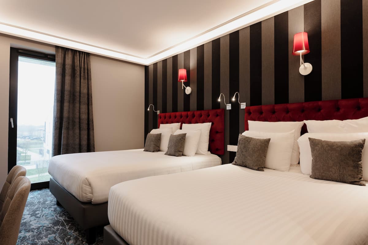 Hotelkamer met twee bedden, gestreept behang, een rode hoofdbord en uitzicht op de stad.
