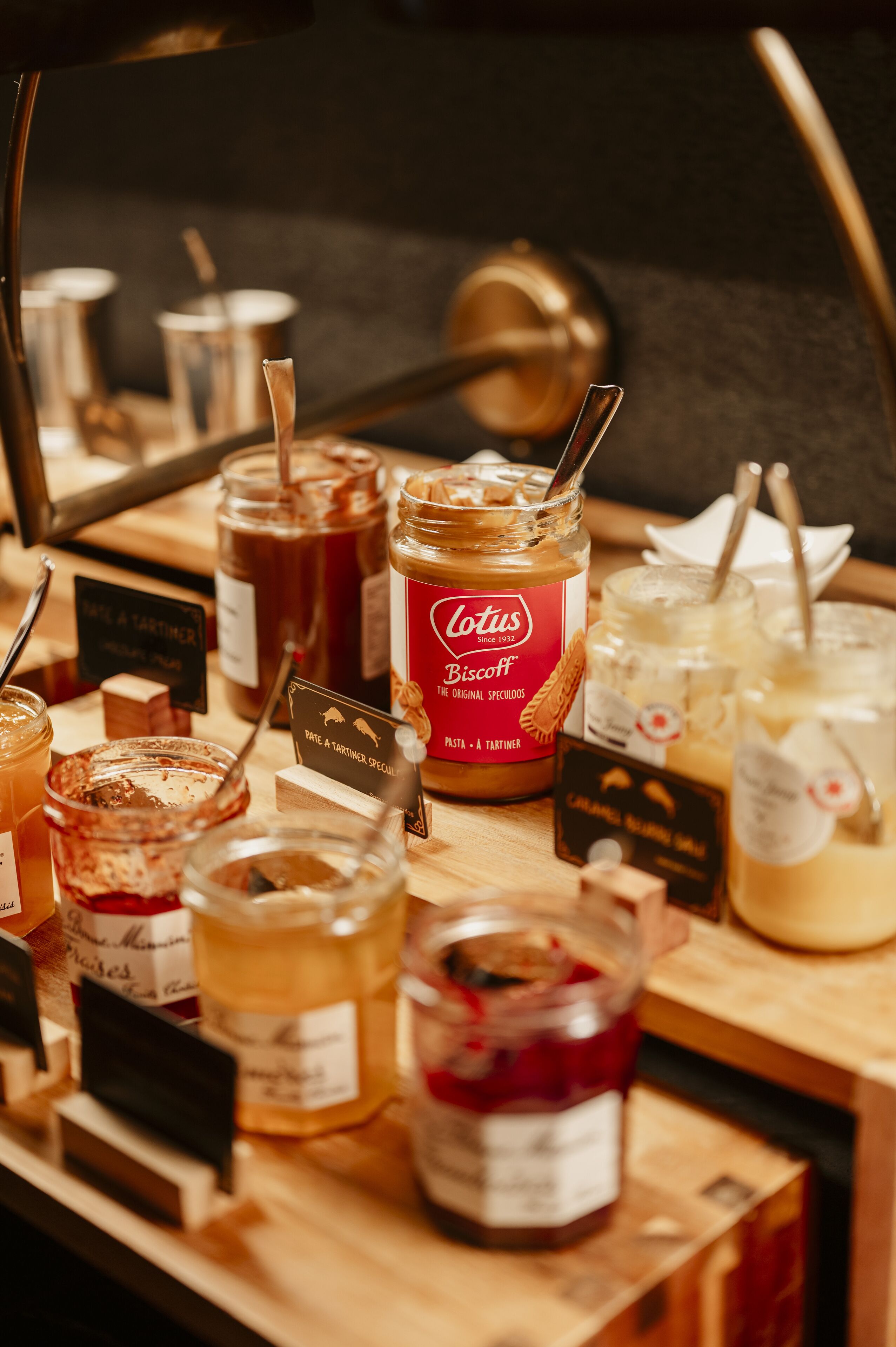 A variety of jars and containers with labels, likely containing food items or condiments, arranged on a wooden surface.