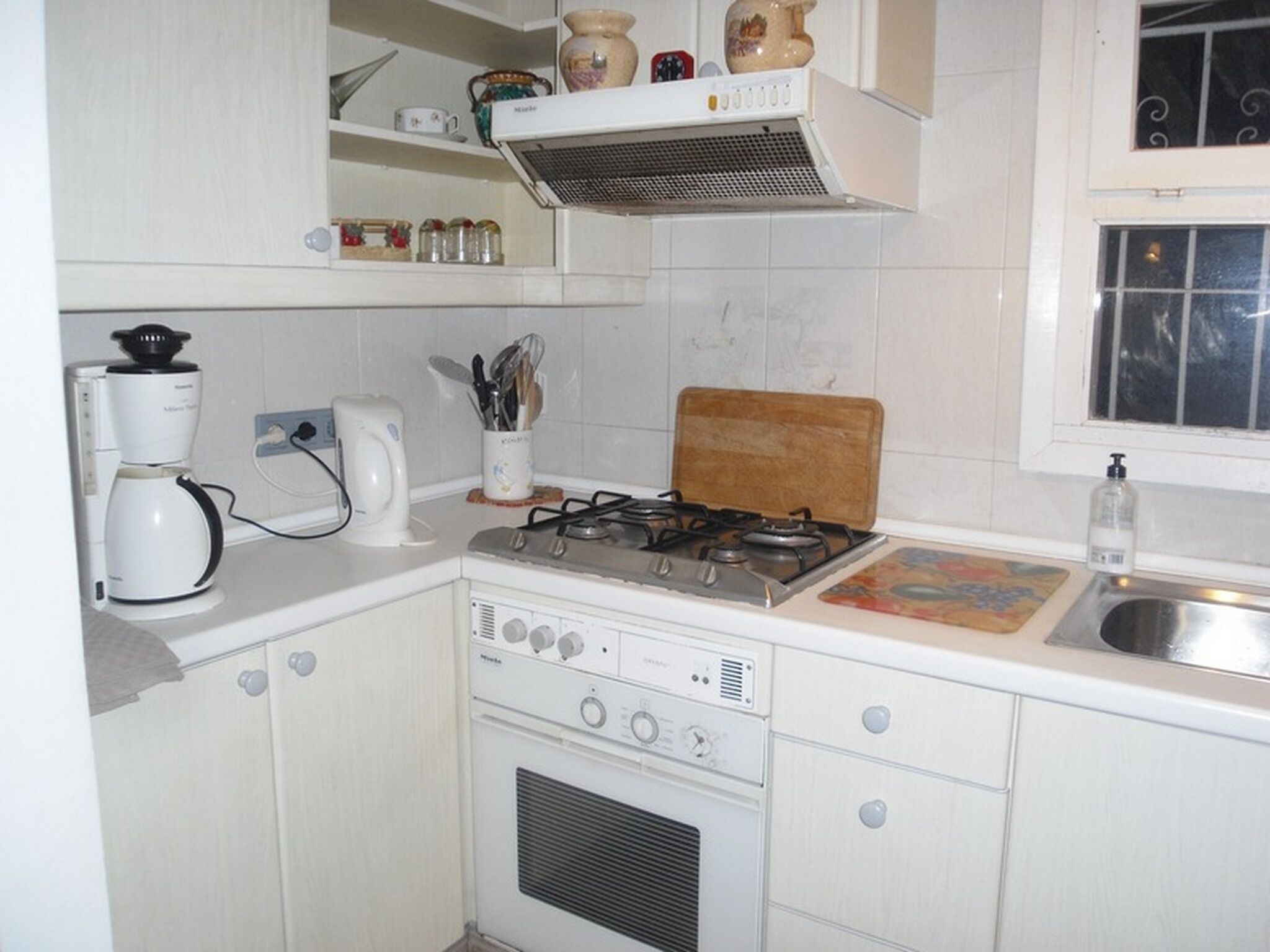 Une cuisine de taille réduite avec des meubles blancs, une cuisinière à gaz, une machine à café et un grille-pain.
