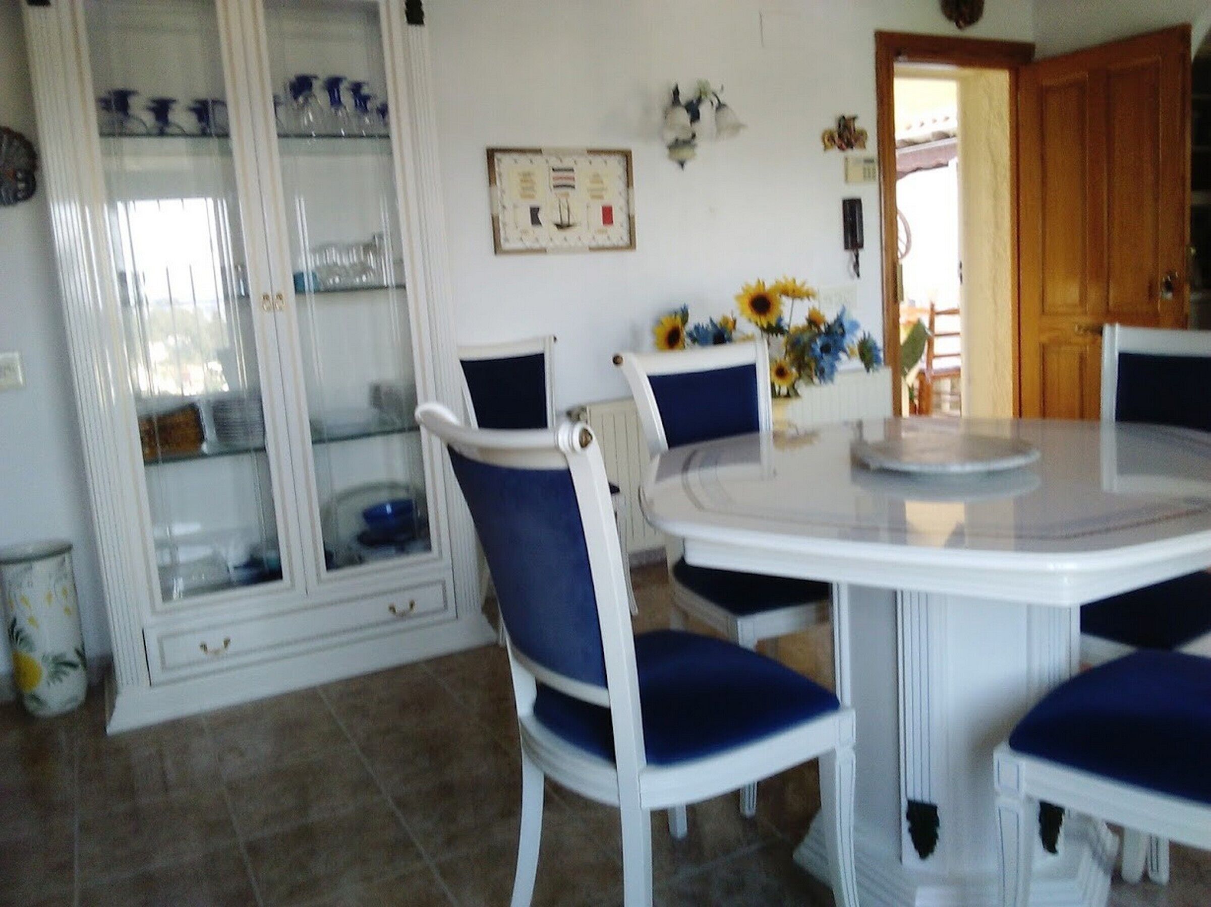 A dining area with a round table, white chairs with blue cushions, and a glass cabinet with blue items.