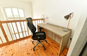 Une pièce avec un bureau en bois, un fauteuil de bureau noir, un lampadaire et une fenêtre donnant sur un beau paysage.