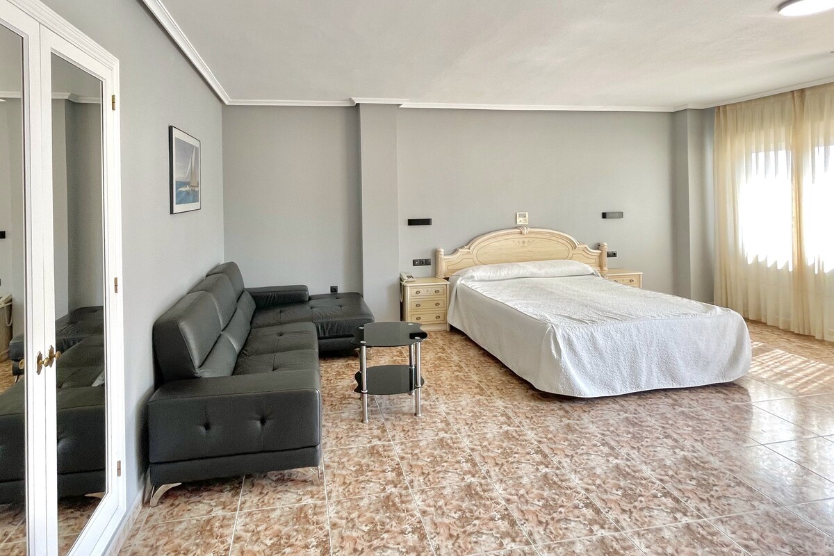 A bedroom with a bed, a sofa, a nightstand, and a mirror.