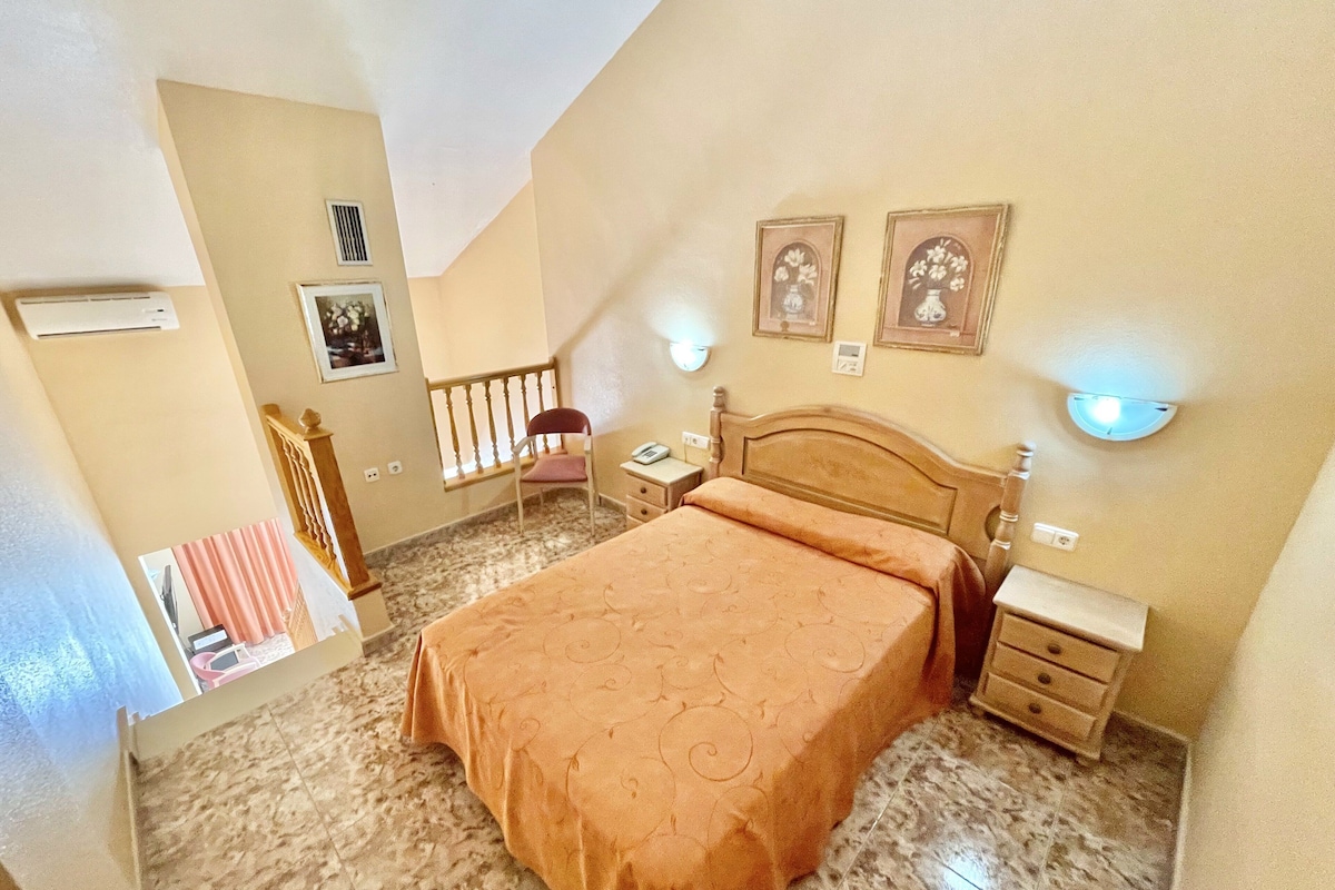 A bedroom with a bed, bedside tables, a chair, a desk, and a window with curtains.