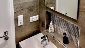 Un bany amb una paret de fusta, un lavabo blanc, un mirall i un dosificador de sabó.