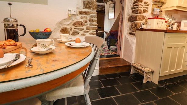 Eine gemütliche Küche mit Steinwand, einem Holztisch mit Frühstücksutensilien und einer kleinen Stufe, die zu einer Treppe führt.
