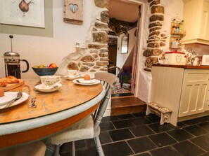 A cozy kitchen with a stone wall, a wooden table with breakfast items, and a small step leading to a staircase. - Duckdown (Clitheroe)