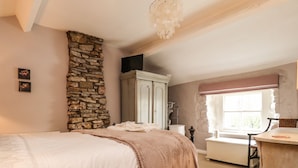 Ein Schlafzimmer mit einer Steinsandsteinwand, einem Bett mit weißer und beiger Bettdecke, einer hölzernen Kommode und einem Fenster mit rosa Vorhang.