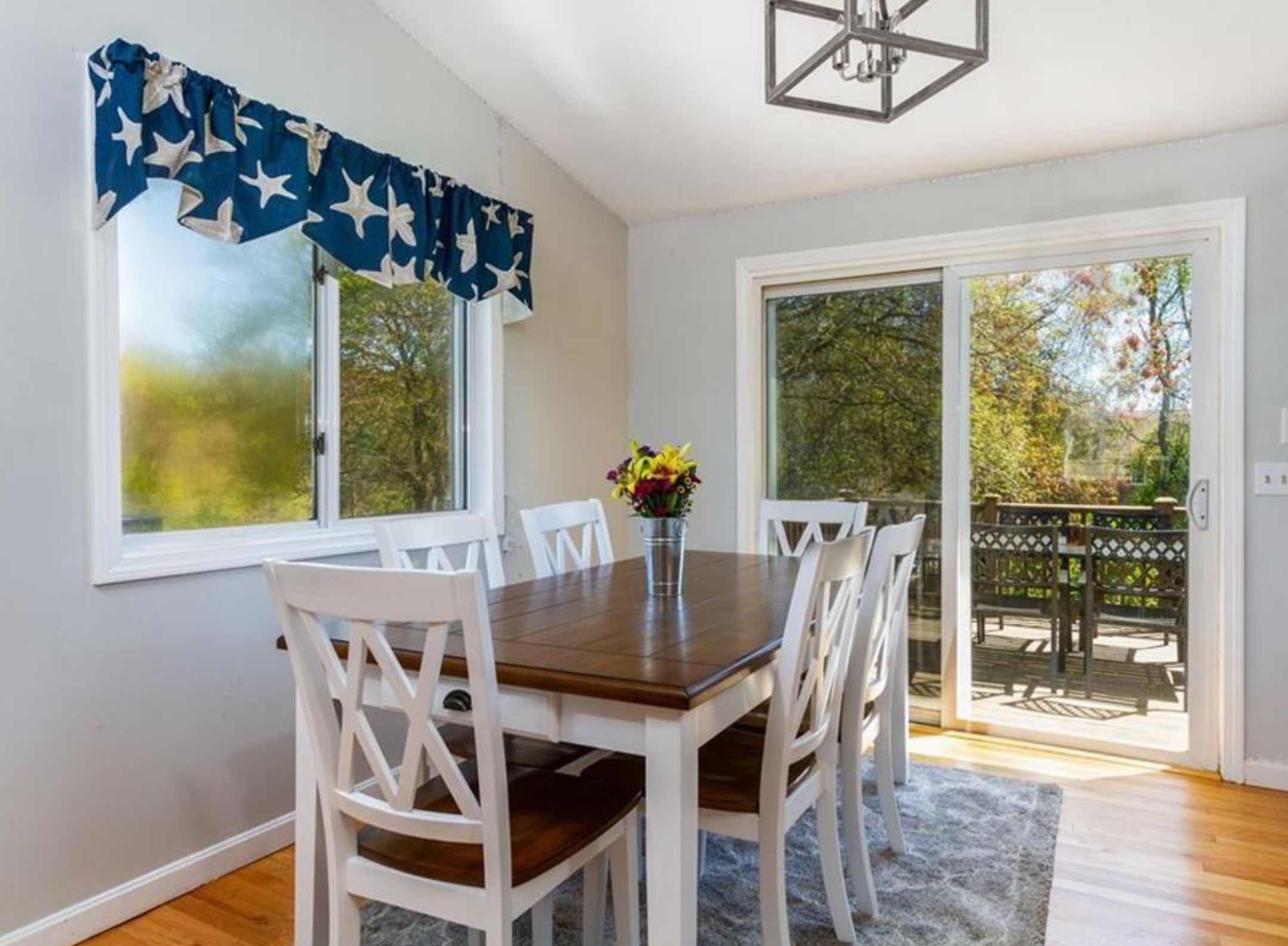 A dining area with a table, chairs, a vase with flowers, and a view of the outdoors through a sliding door.