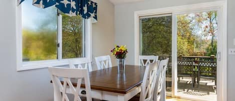 Un coin repas comprenant une table, des chaises, un vase avec des fleurs et une vue sur l’extérieur grâce à une porte coulissante.