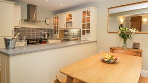 A modern kitchen with a wooden dining table, a built-in oven, and a large window. - 2 Kings Yard (Sedbergh)