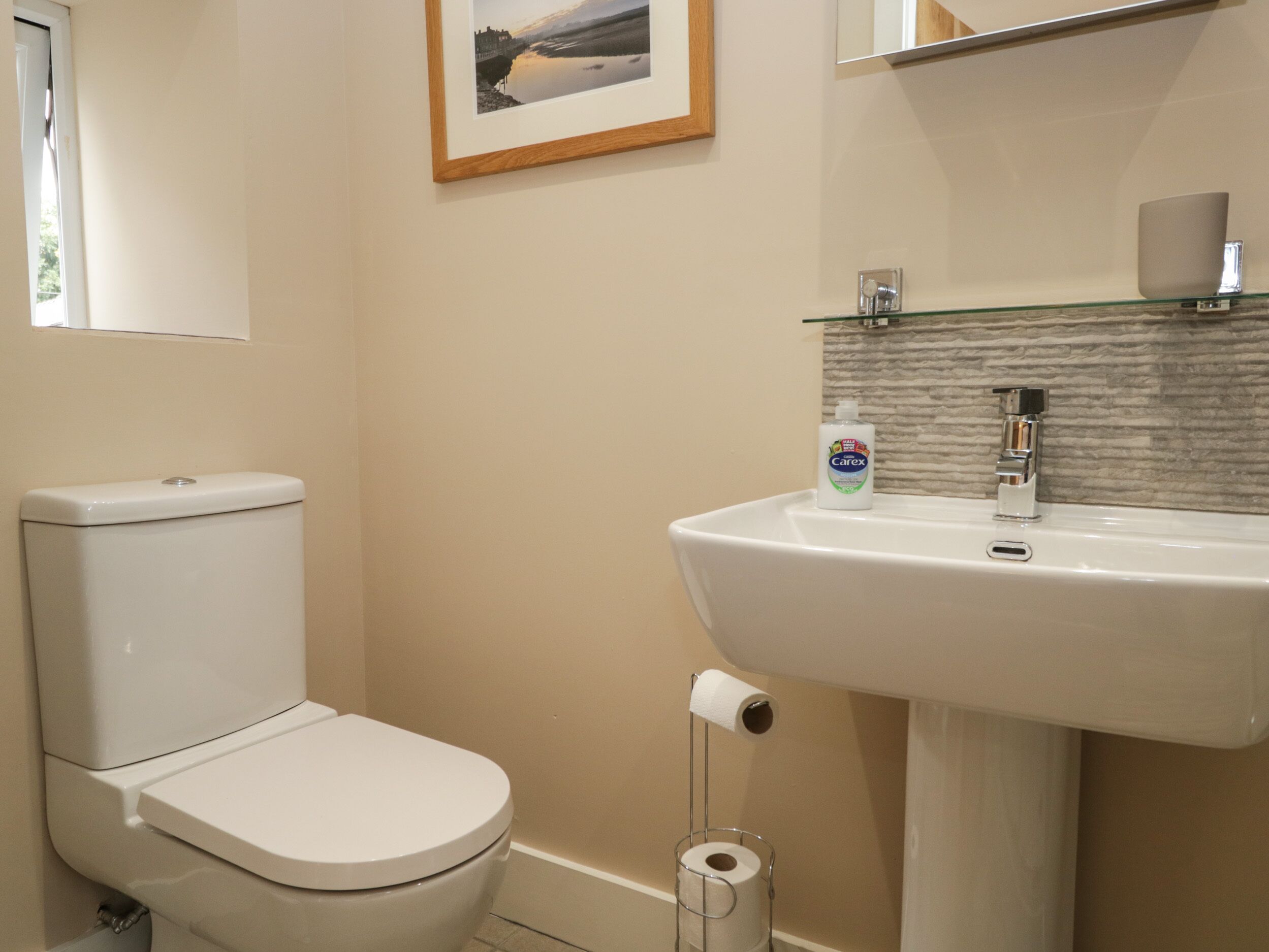 Een badkamer met een toilet, een wastafel, een lijst met een foto aan de muur en een toiletrolhouder.