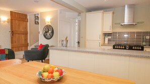 A modern kitchen with a wooden dining table, a fruit bowl, and a built-in stove. - 2 Kings Yard (Sedbergh)