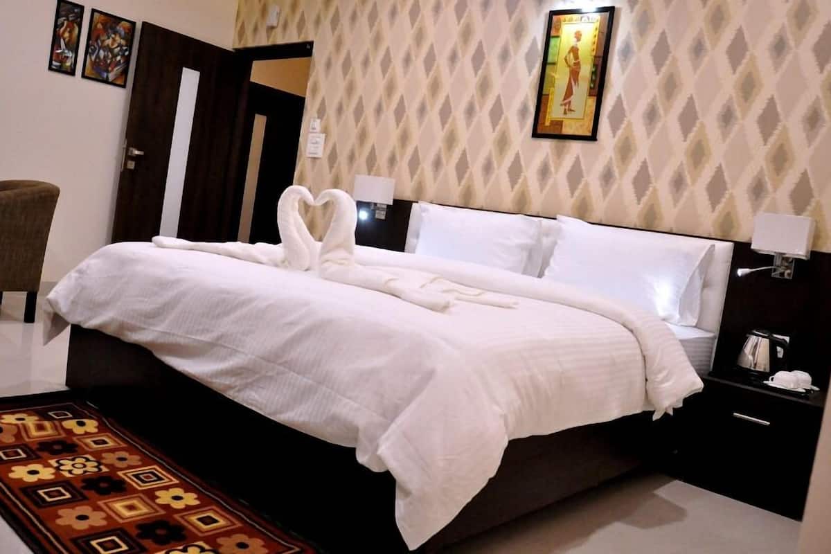 A neatly made bed with white linens and a heart-shaped towel arrangement, a patterned rug, and a nightstand with a lamp and a phone.