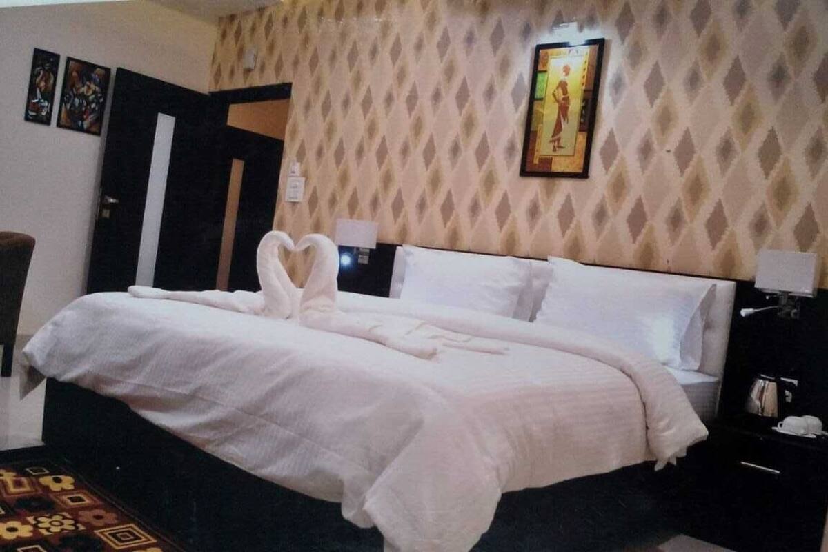 A neatly made bed with white linens and two heart-shaped towels.