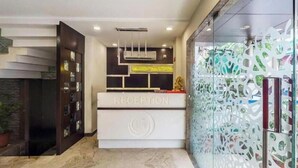 Zona de recepción con mostrador identificado como “RECEPTION”, unidad de aire acondicionado moderna y separador de vidrio decorativo con patrones abstractos.