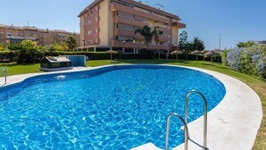 A swimming pool with a clear blue water surface, surrounded by a concrete deck. In the background, there is a multi-story building with balconies and a flat roof. - Duplex Algarrobo Costa Solset (Algarrobo)