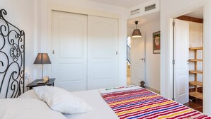 A bedroom with a bed, a bedside table with a lamp, a colorful striped rug, and a wardrobe. - Duplex Algarrobo Costa Solset (Algarrobo)