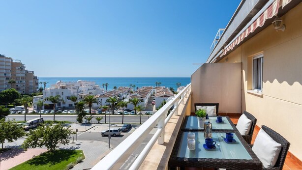 A balcony with a glass table and chairs, overlooking a coastal street and buildings, with a clear view of the sea. - Duplex Algarrobo Costa Solset (Algarrobo)