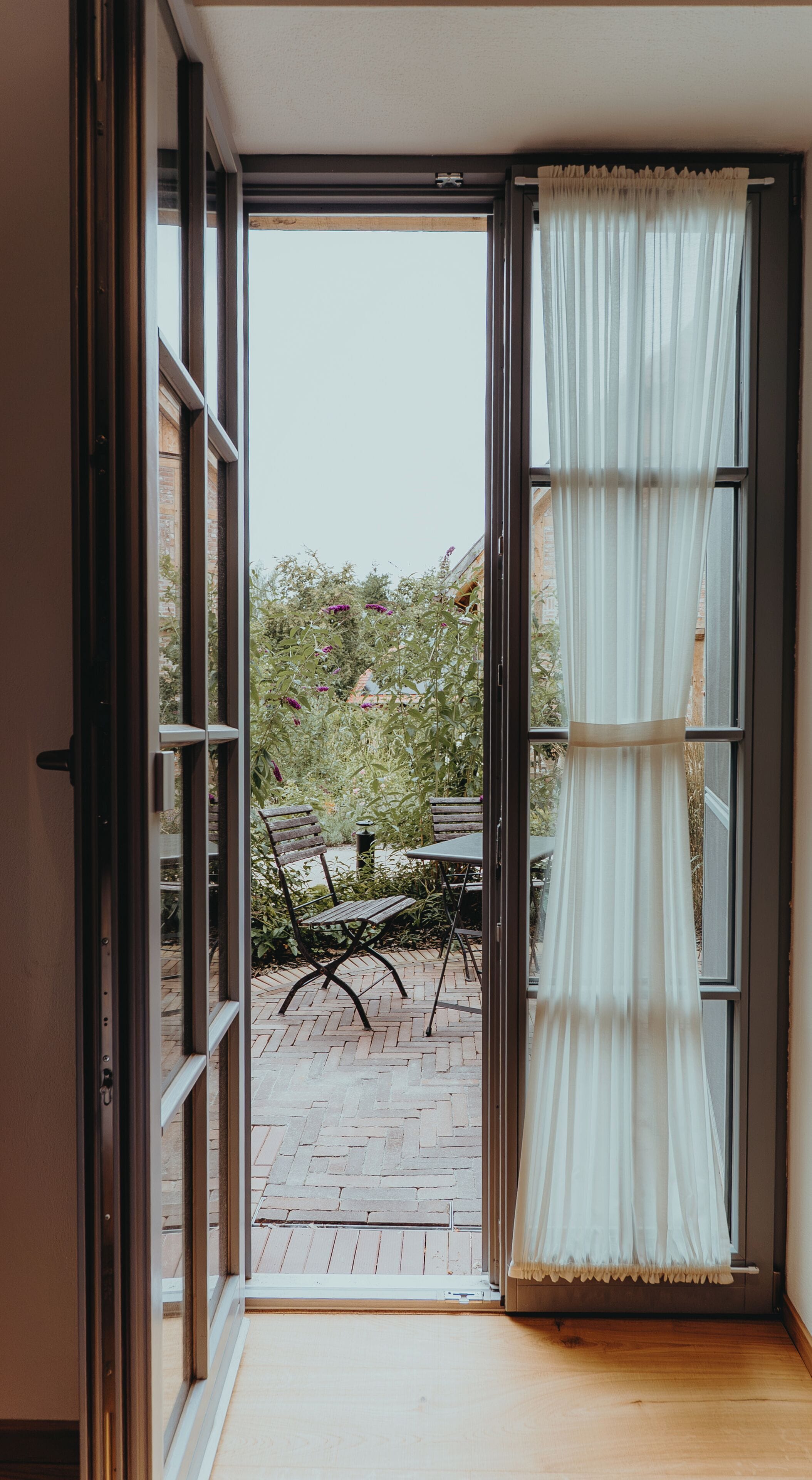 Puerta corredera de vidrio abierta que da a un patio exterior con suelo de ladrillo y una mesa con sillas.