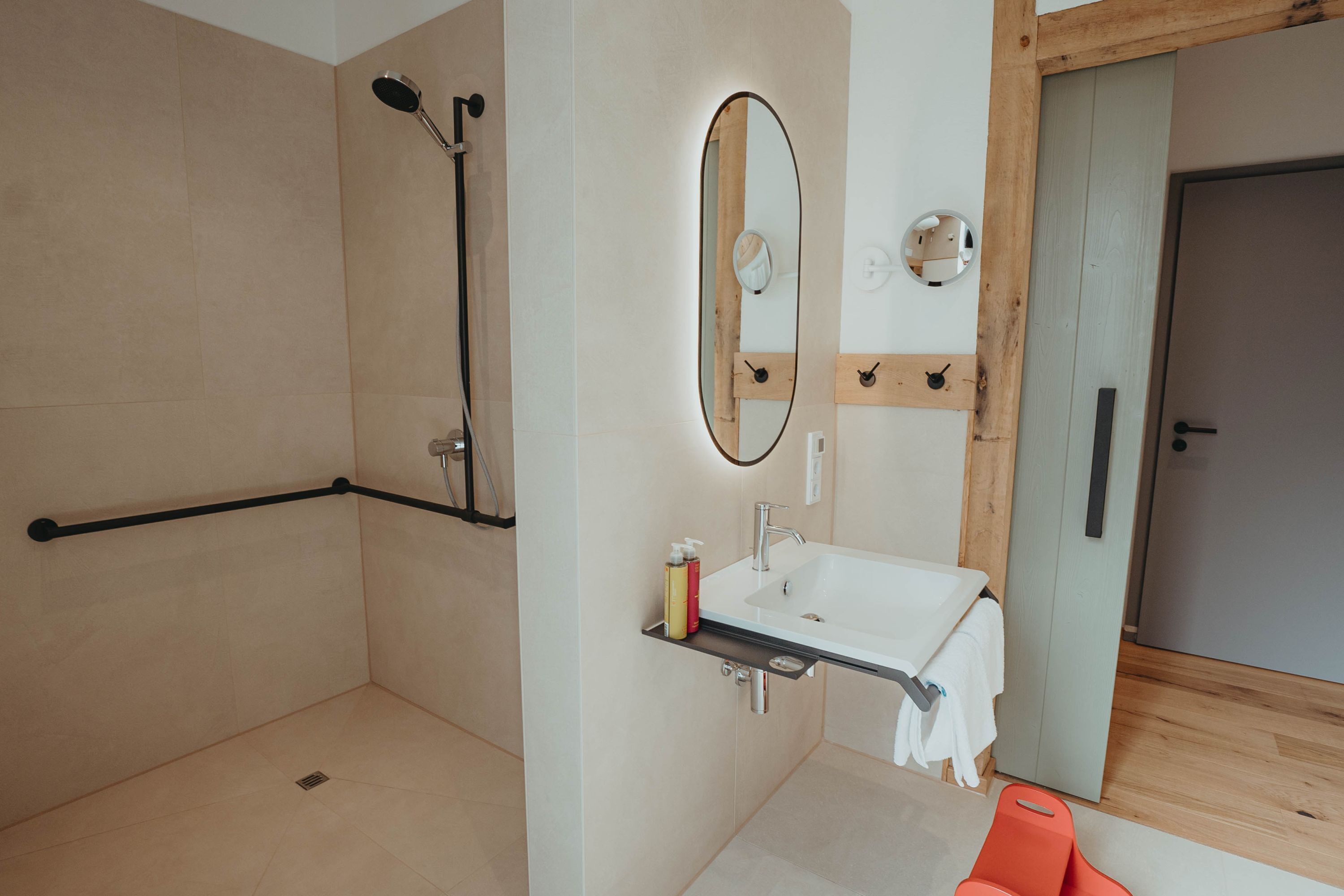 Un baño moderno con ducha a ras de suelo, un lavabo con espejo y un perchero para toallas.